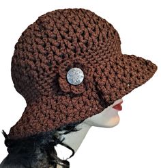 a brown crocheted hat with a button on the front and side, sitting on top of a mannequin's head