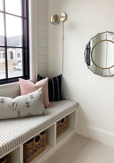 a window seat with some pillows on it and a mirror hanging above the windowsill