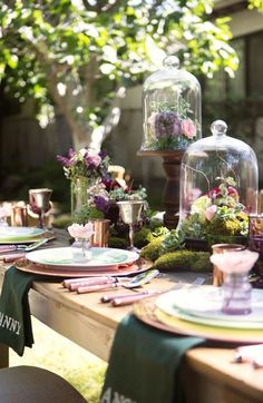 the table is set with plates, cups and vases filled with flowers on them