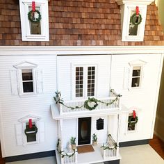 a white doll house with wreaths on the front and windows, decorated for christmas