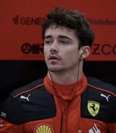 a man with headphones on sitting in front of a red sign and wearing a black jacket