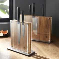 three knives are sitting on top of the wooden block in front of a window with an orange slice