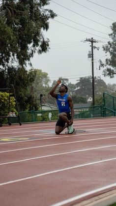 a man kneeling down on top of a race track with his hands in the air