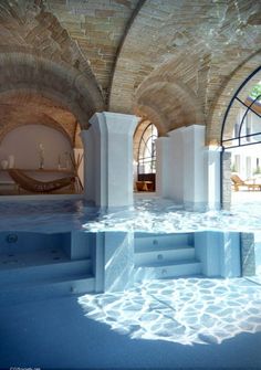 an indoor hot tub in the middle of a room with stone walls and arched windows