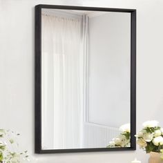 a black framed mirror sitting on top of a white wall next to a vase with flowers