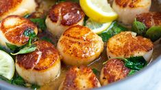 some scallops are cooking in a pan with lemon wedges and spinach