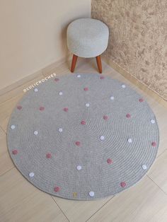 a round rug with white and pink dots on it next to a small stool in a corner