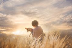 a boy and his dog are standing in tall grass at sunset with the sun behind them