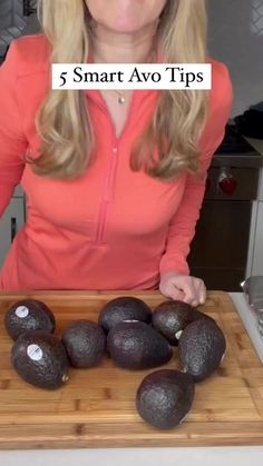 a woman standing in front of a cutting board with avocados on it