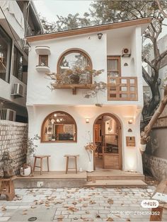 a white house with lots of windows and plants on the front porch, next to a tree