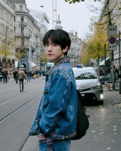 a young man standing on the side of a road next to a street with cars and people