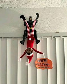 an elf hanging upside down from the ceiling next to a sign with help written on it