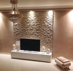 a living room with a television and chandelier hanging from the ceiling, in front of a stone wall