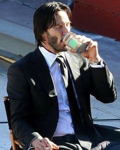 a man in a suit and tie drinking from a cup while sitting on a chair