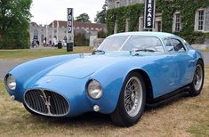 an old blue sports car parked in front of a house