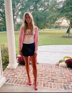 a woman standing in front of a porch wearing pink and white shirt, black miniskirt