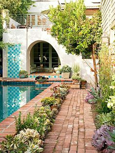 an outdoor swimming pool surrounded by greenery and brick pavers path leading to the patio