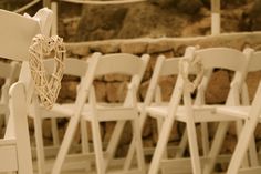 rows of white wooden chairs with heart decorations on the back and sides, lined up against a stone wall