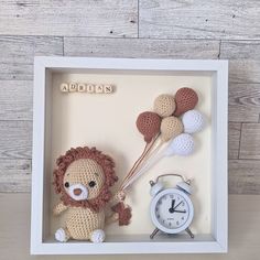 a crocheted lion in a shadow box with balloons and a small alarm clock