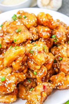 a white plate topped with chicken covered in sesame seeds and garnished with green onions