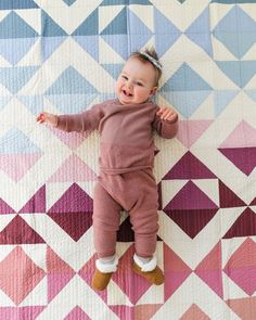 a baby laying on top of a quilt with her hands in the air and smiling