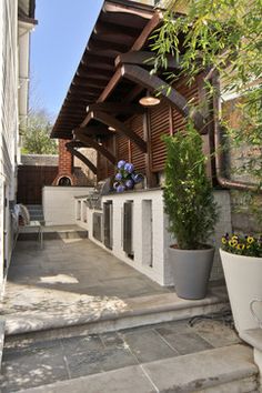 an outdoor kitchen and grill area with potted plants on the side of the building