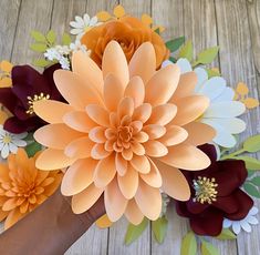 a hand holding an orange flower on top of a wooden table next to other flowers