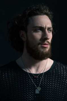 a man with long hair and a beard wearing a black shirt is looking off to the side