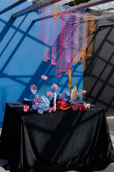 a black table topped with flowers and paper cranes hanging from it's ceiling next to a blue wall