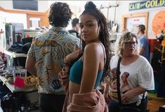 a woman standing in front of a counter with people behind her looking at the camera