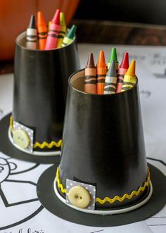 two black cups with crayons in them sitting on top of a table