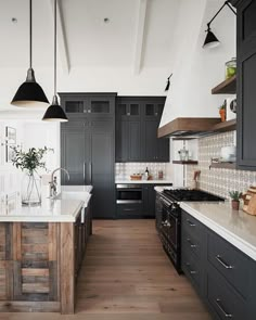 a large kitchen with black cabinets and white counter tops, wood flooring and pendant lights hanging from the ceiling