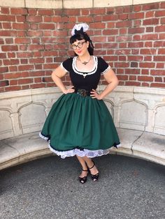 a woman in a green dress and black top standing next to a red brick wall