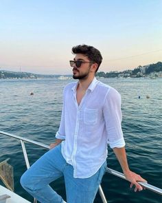 a man standing on top of a boat near the ocean with his hands in his pockets