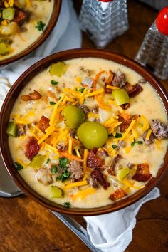 two bowls of soup with cheese, olives and bacon on the side next to a glass of water