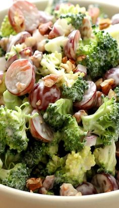 a salad with broccoli, grapes and nuts in a white bowl on a table