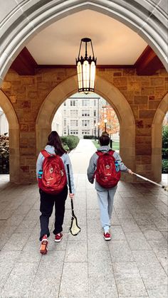 two people walking down a walkway with backpacks and tennis rackets in their hands