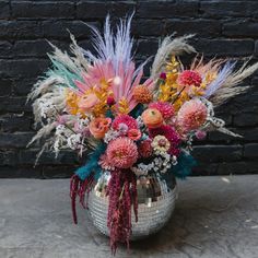 a disco ball vase filled with lots of colorful flowers and feathers in front of a brick wall