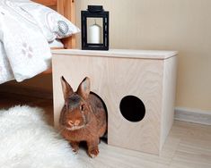 a small rabbit is sitting in the corner of a wooden box next to a bed