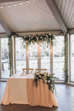 a table with flowers and greenery is set up in front of a large window