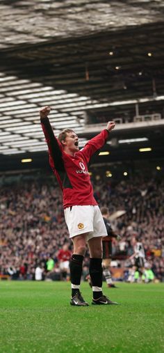 a man in red and white uniform standing on soccer field with his arms up to the sky