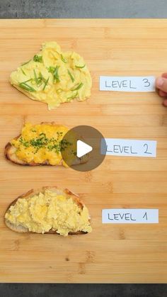 a wooden cutting board topped with three pieces of bread covered in different types of food