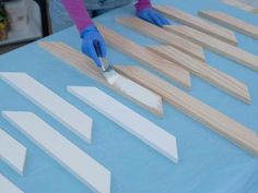 a person in blue gloves is painting wooden strips on a table with white paint and wood planks