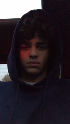 a man in a hoodie looking at his cell phone with an angry look on his face