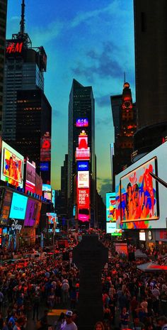 a crowded city street filled with lots of people and tall buildings at night time, all lit up