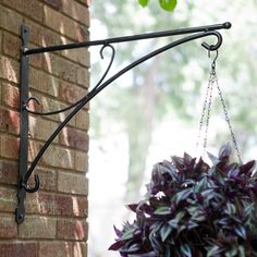 a potted plant is hanging from a black iron bracket on the side of a brick building