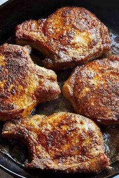 four pieces of meat cooking in a skillet