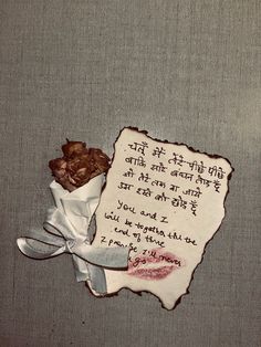 a piece of paper with writing on it next to a rose and ribbon tied around it