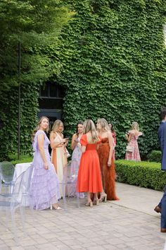 a group of people standing around each other in front of a green wall with ivy growing on it