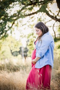 a pregnant woman in a red dress standing in tall grass